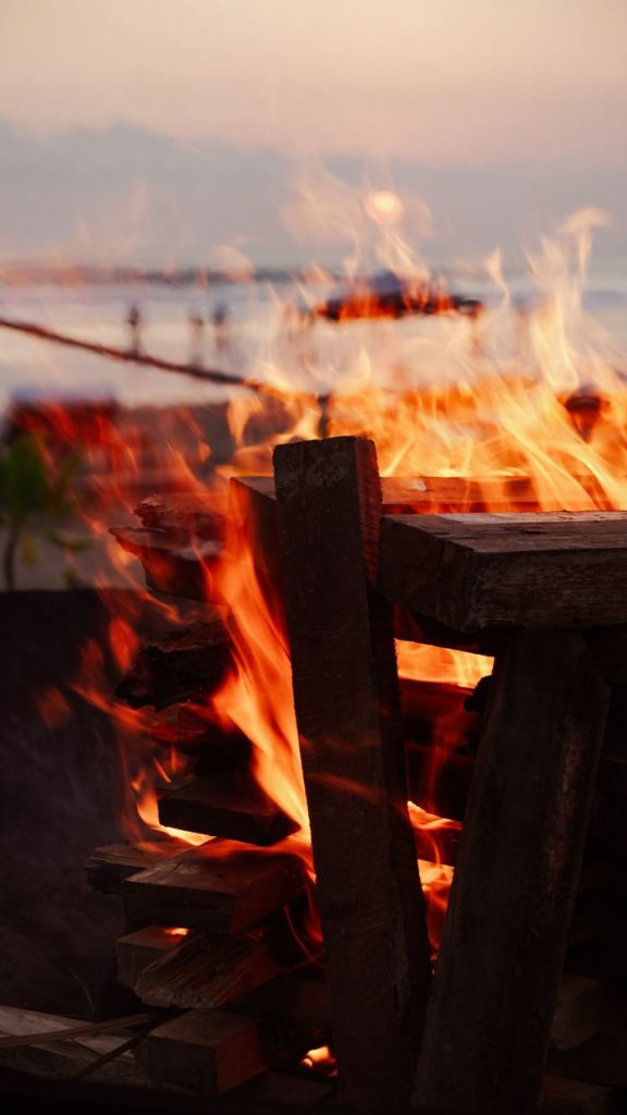 Warm bonfire on a beach creating a vibrant glow at sunset.