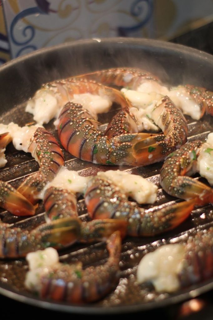 Succulent lobster tails grilling with butter and herbs, emitting aromatic steam.